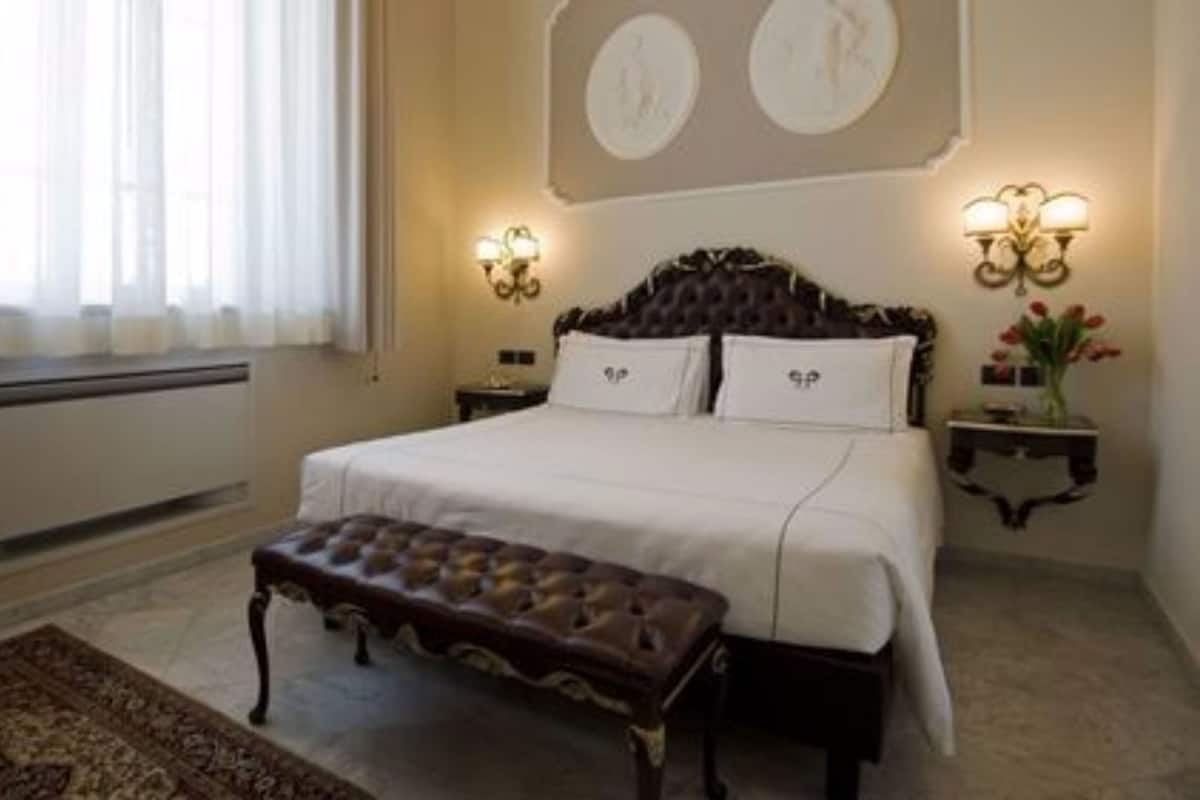 Une chambre d’hôtel avec un grand lit, une banquette, deux appliques murales et un radiateur.