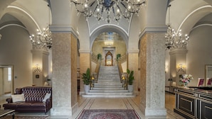 Un vestíbulo imponente con una escalera de mármol, candelabros y un sofá de cuero.