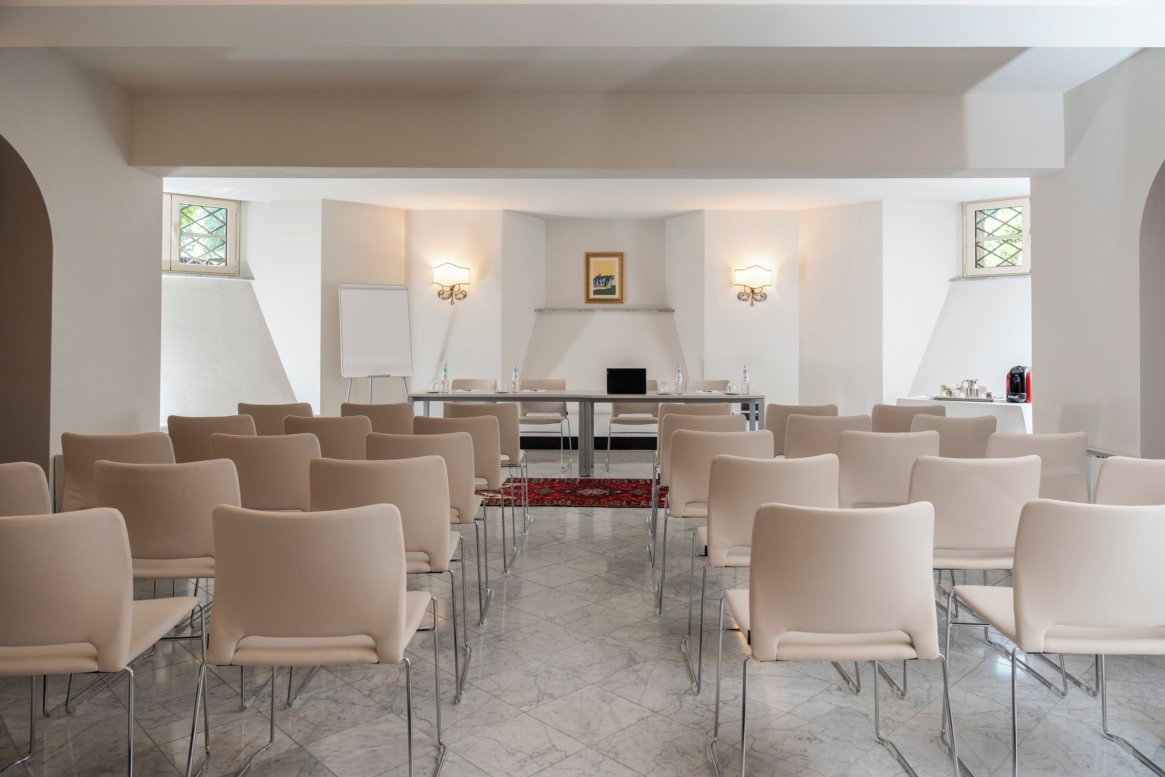 Una sala conferenze con un lungo tavolo, diverse sedie e due lampade a parete.