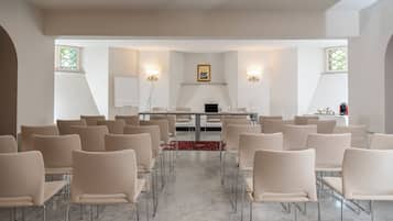Una sala conferenze con un lungo tavolo, diverse sedie e due lampade a parete.