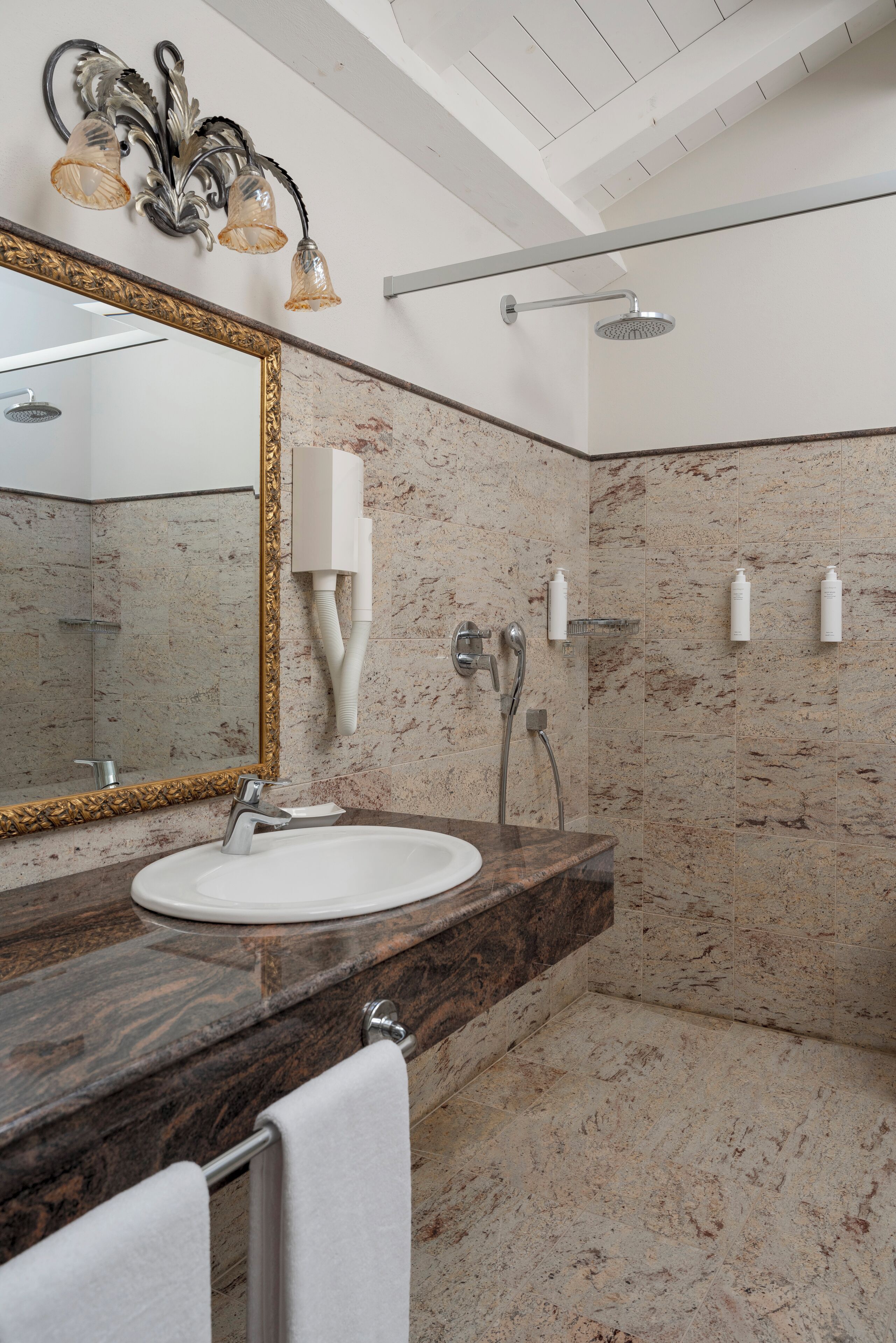 Une salle de bain avec un lavabo en marbre, un grand miroir, une pomme de douche et un porte-serviettes.