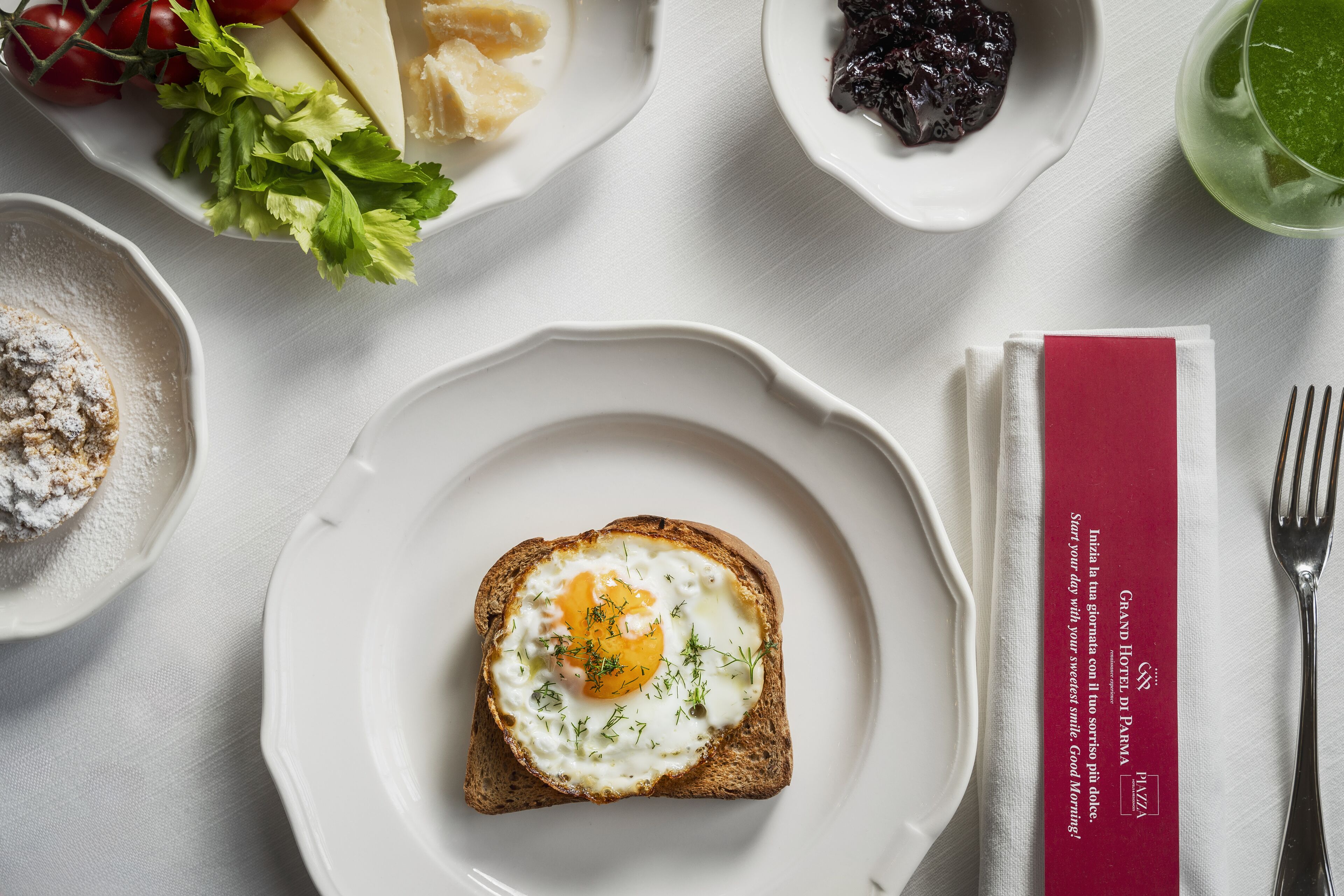 Desayuno con tostadas, huevos y diferentes acompañamientos sobre una mesa blanca.