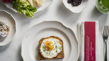 Desayuno con tostadas, huevos y diferentes acompañamientos sobre una mesa blanca.