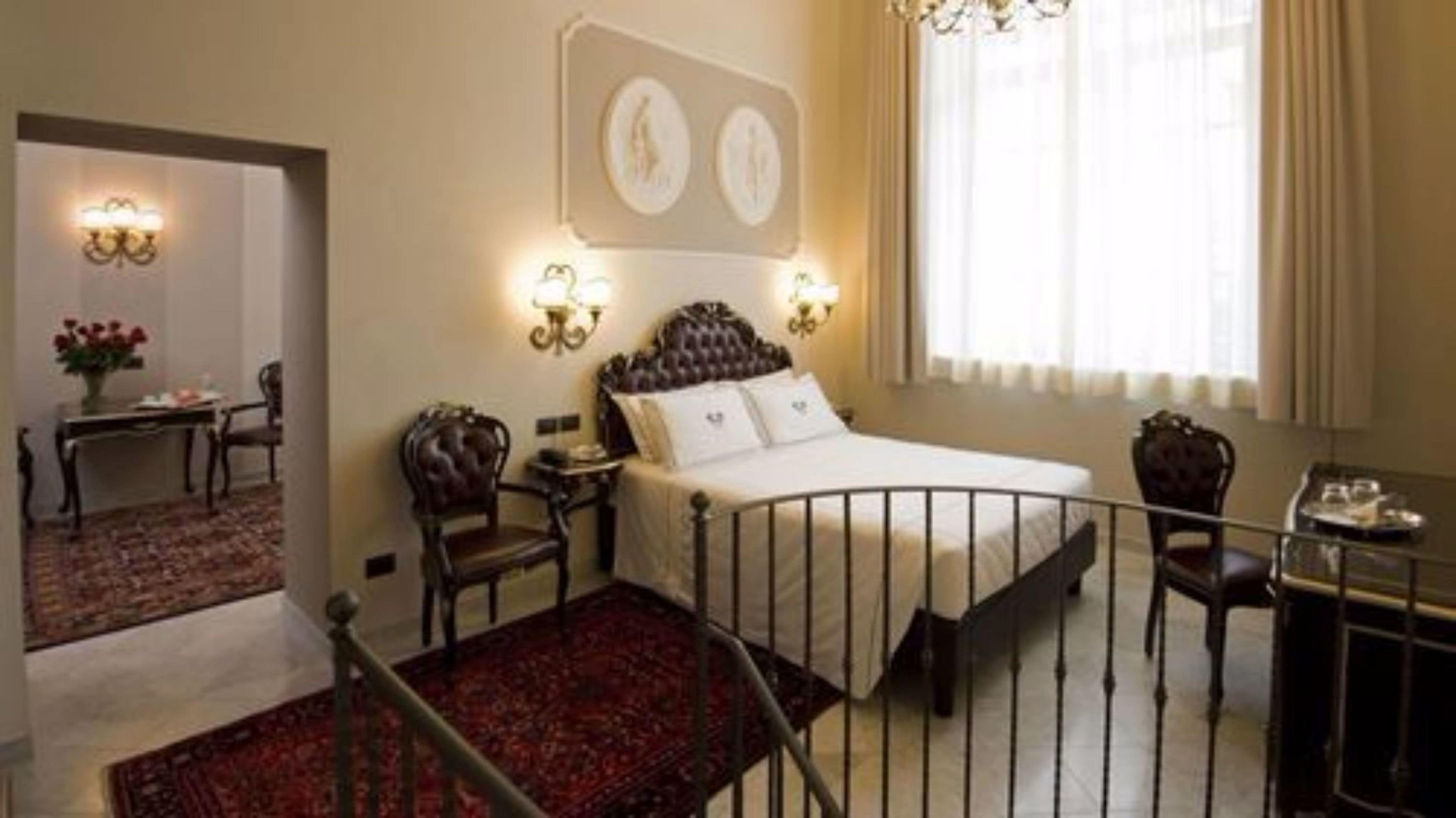 A hotel room with a bed, a desk, a chair, a small table, and a window with curtains.