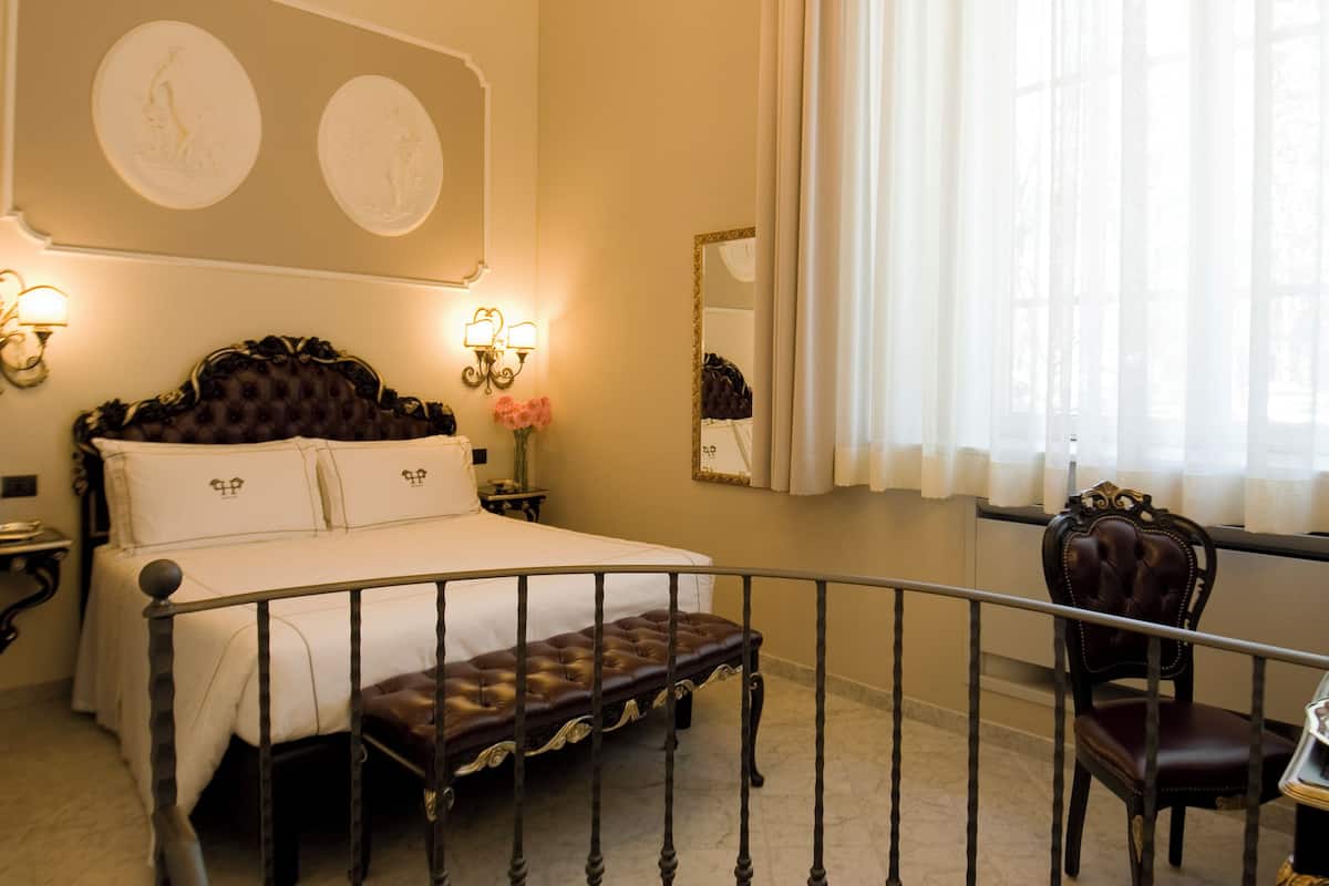 Une chambre à coucher avec un grand lit, un banc, une chaise, une table avec un plateau et une fenêtre avec des rideaux.