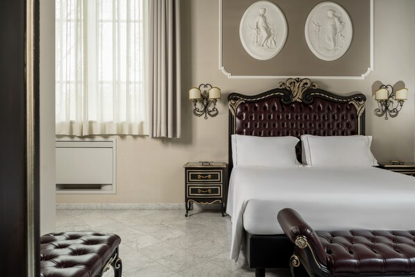 A bedroom with a large bed, a nightstand with drawers, a bench, and two wall-mounted lamps. - Grand Hotel di Parma | UNA Esperienze (Parma)