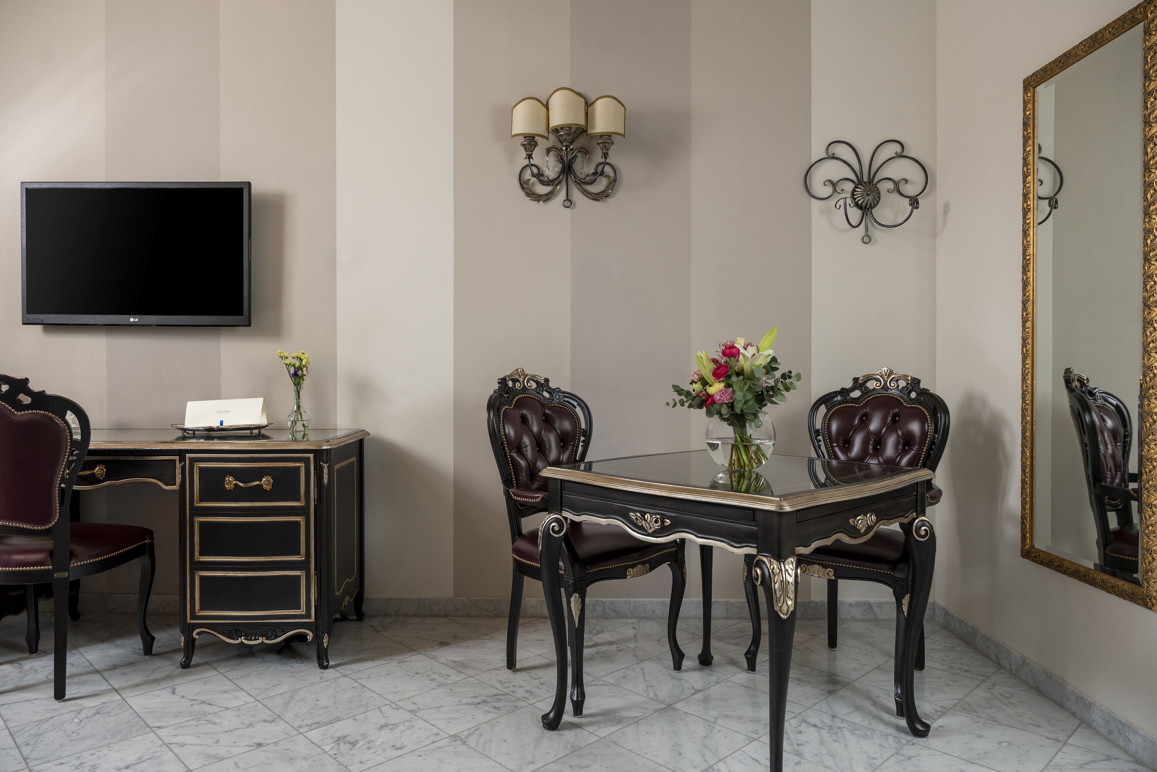 A dining area with a table, chairs, a television, and wall-mounted lighting.