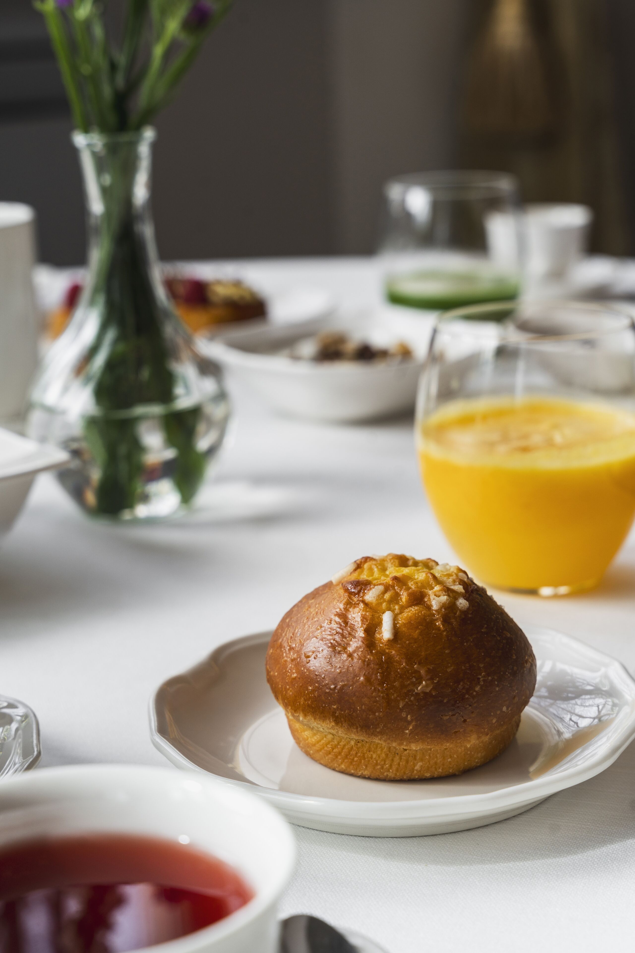 A breakfast setting with a muffin on a plate, a glass of orange juice, and a vase with flowers.