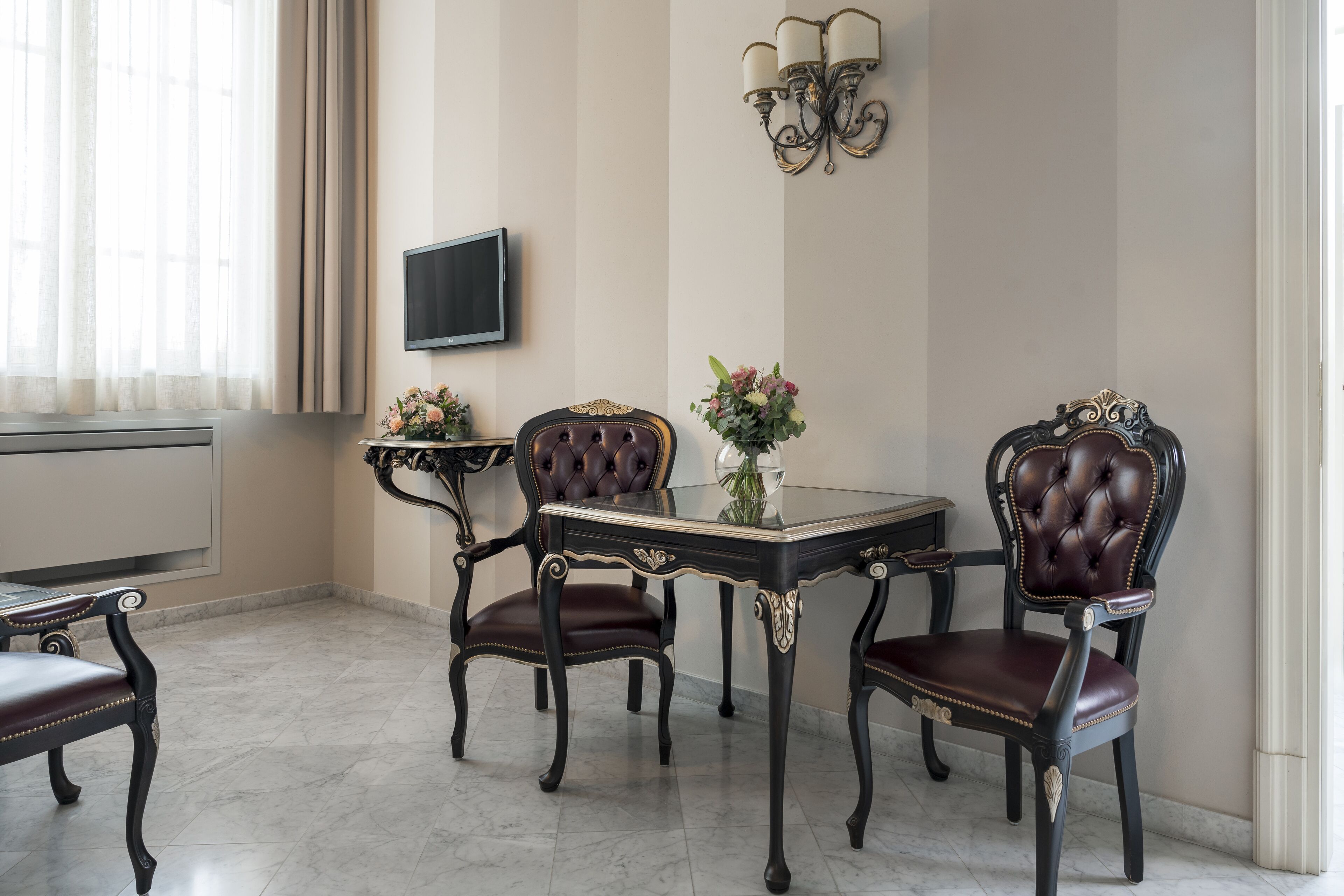 Uma área de refeições com uma mesa e quatro cadeiras, uma televisão de tela plana na parede e um lustre.