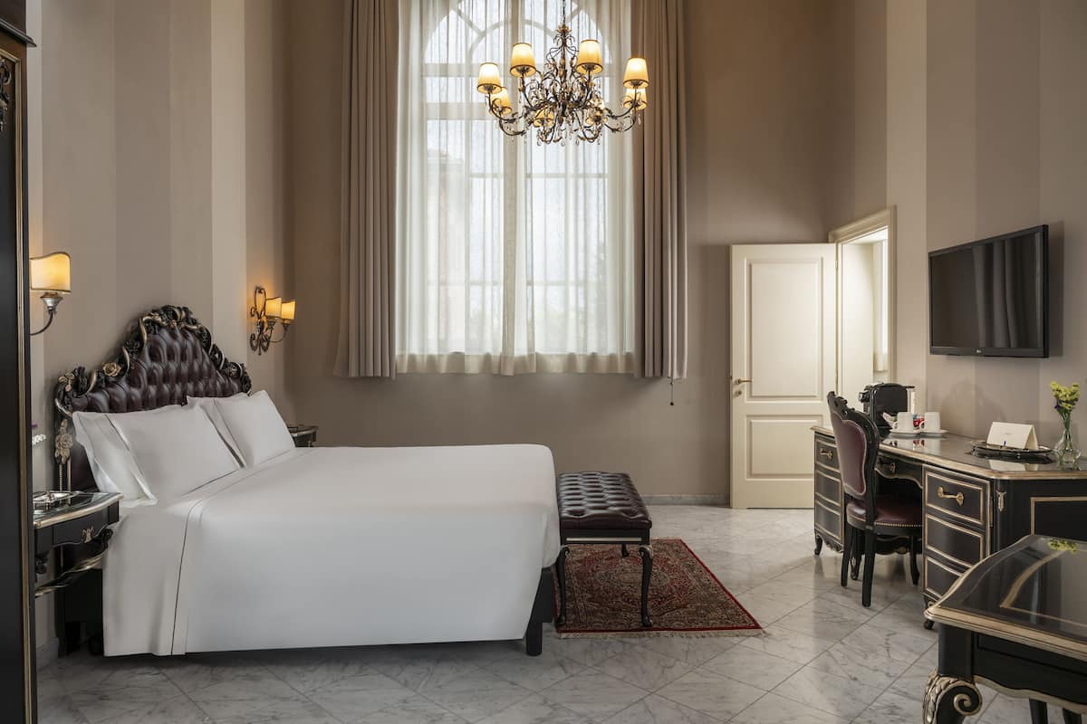 Une chambre d’hôtel avec un grand lit, un bureau, une chaise, une télévision et un lustre.