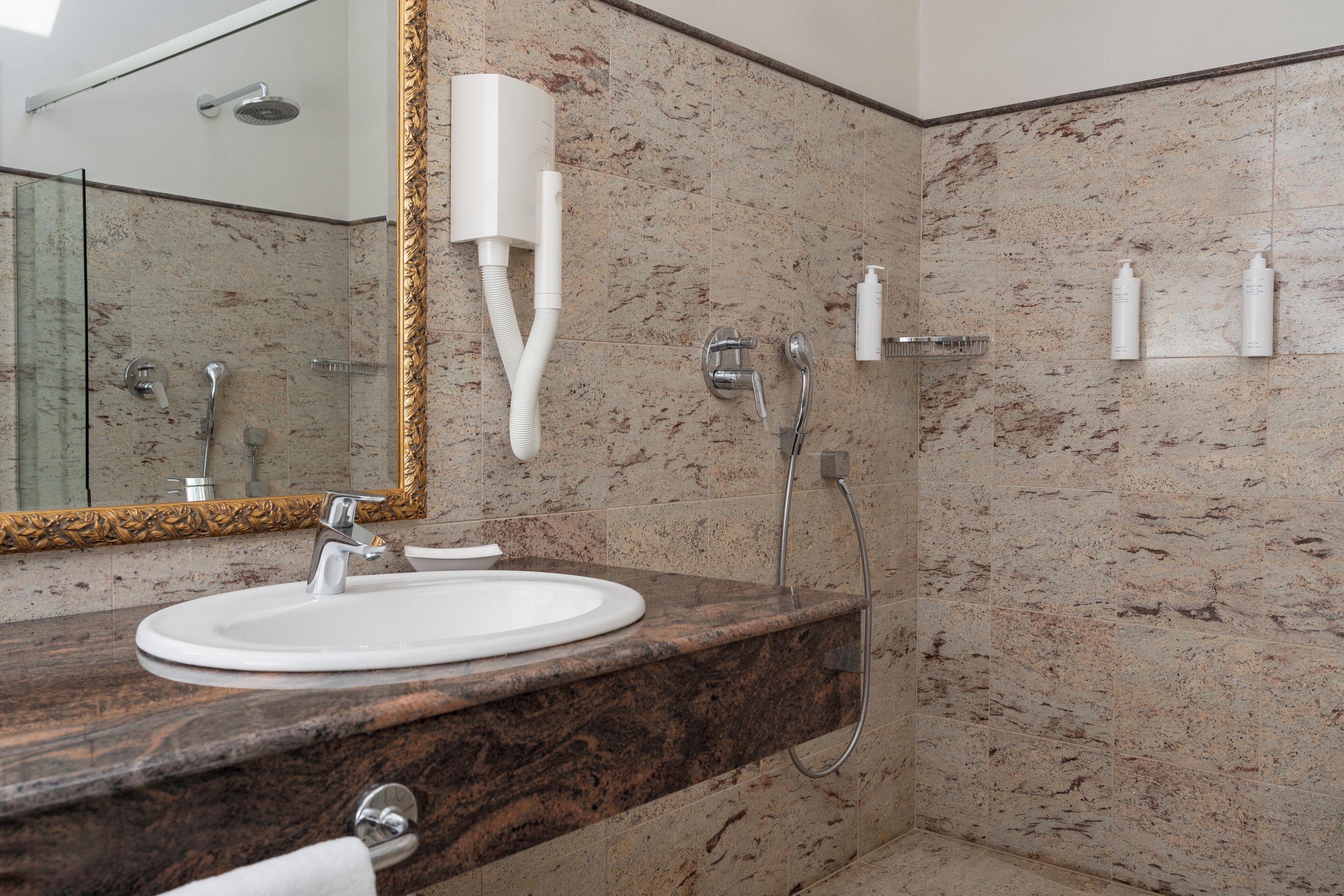 A bathroom with a marble sink, a mirror with a gold frame, and a shower area.