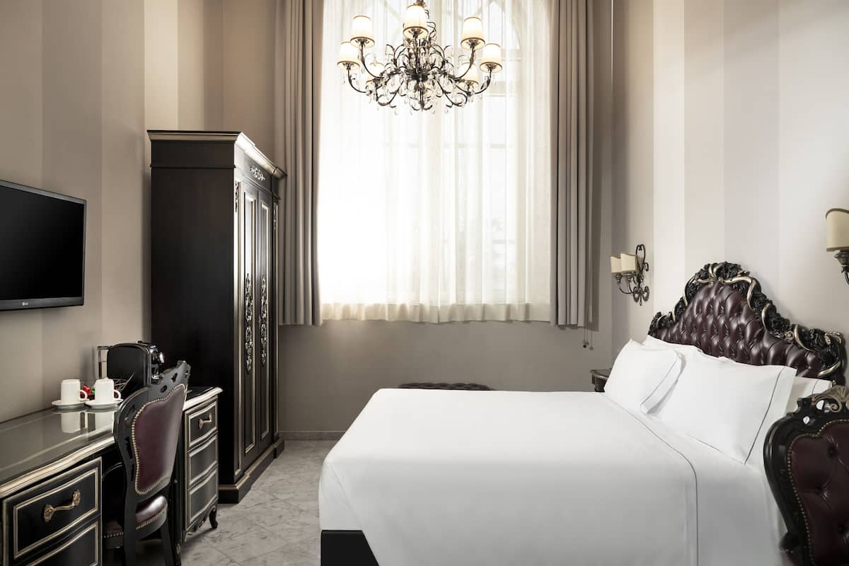 Une chambre d’hôtel avec un grand lit, une télévision, un bureau avec une chaise et une armoire.