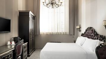 A hotel room with a large bed, a television, a desk with a chair, and a wardrobe.