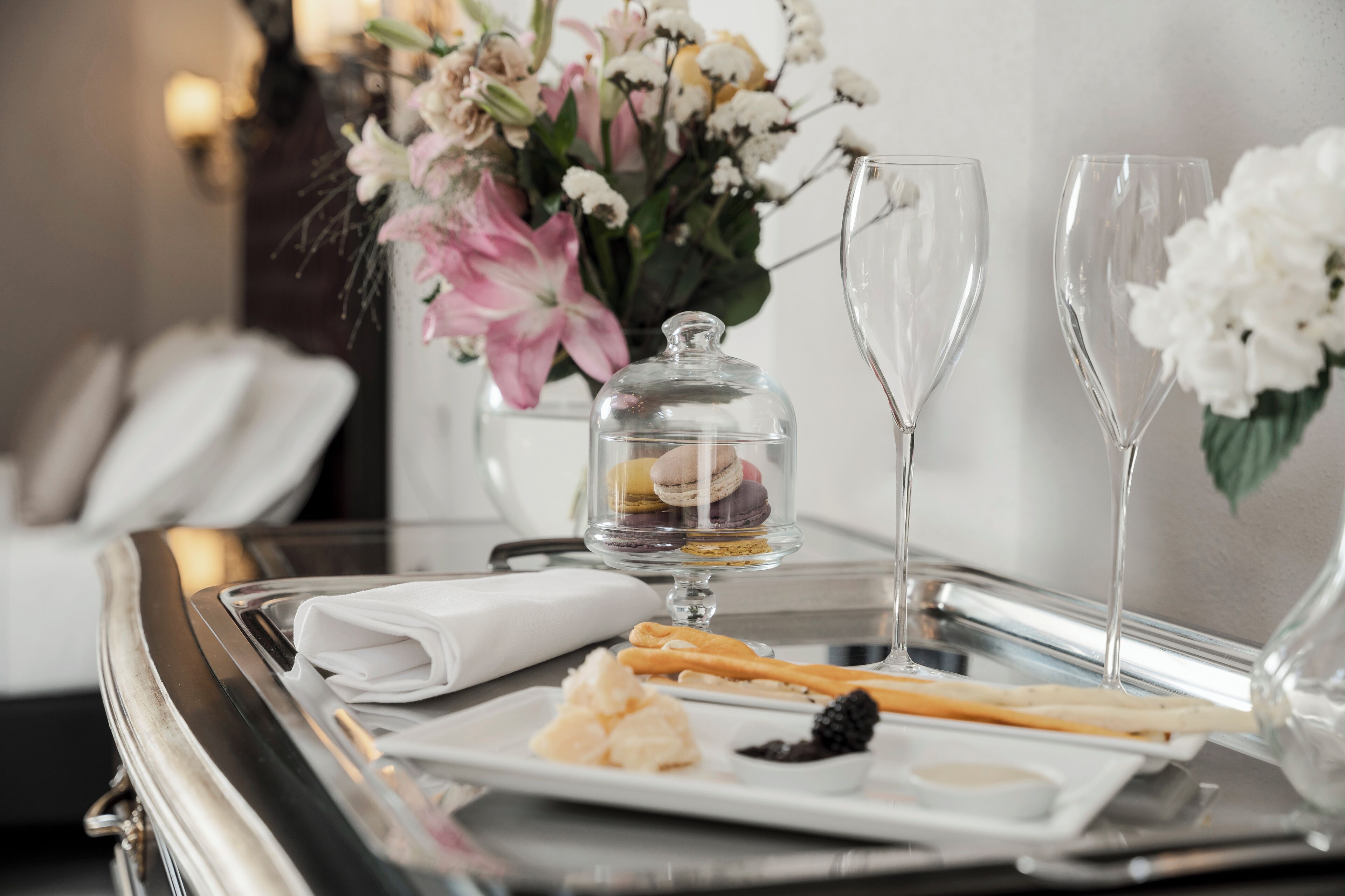Un vassoio con una cupola di vetro che contiene macarons, due flute da champagne, un tovagliolo bianco piegato e un piatto con pasticcini assortiti e una piccola ciotola di cioccolato.