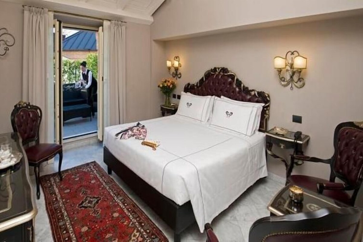 Habitación de hotel con cama, escritorio, silla, mesita de noche y vista al exterior.