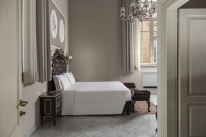 A bedroom with a large bed, a dresser, a chair, and a chandelier. - Grand Hotel di Parma | UNA Esperienze (Parma)