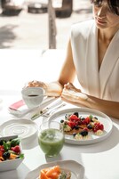 Una mesa de comedor con una fuente de panqueques cubiertos de bayas, un vaso de jugo verde y un tazón de fruta mixta.