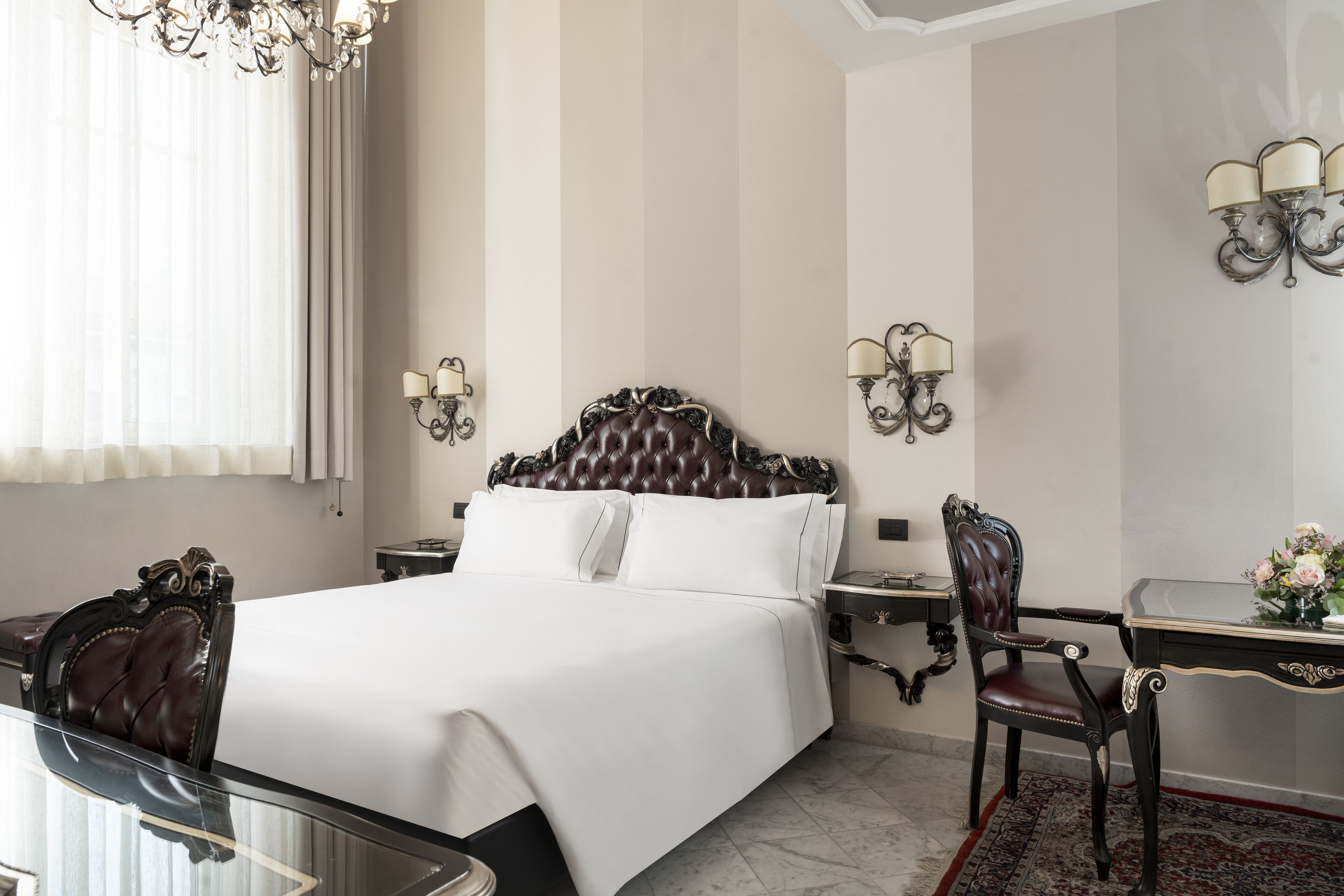 Une chambre d’hôtel avec un grand lit, un bureau avec une chaise, un lustre et des appliques murales.
