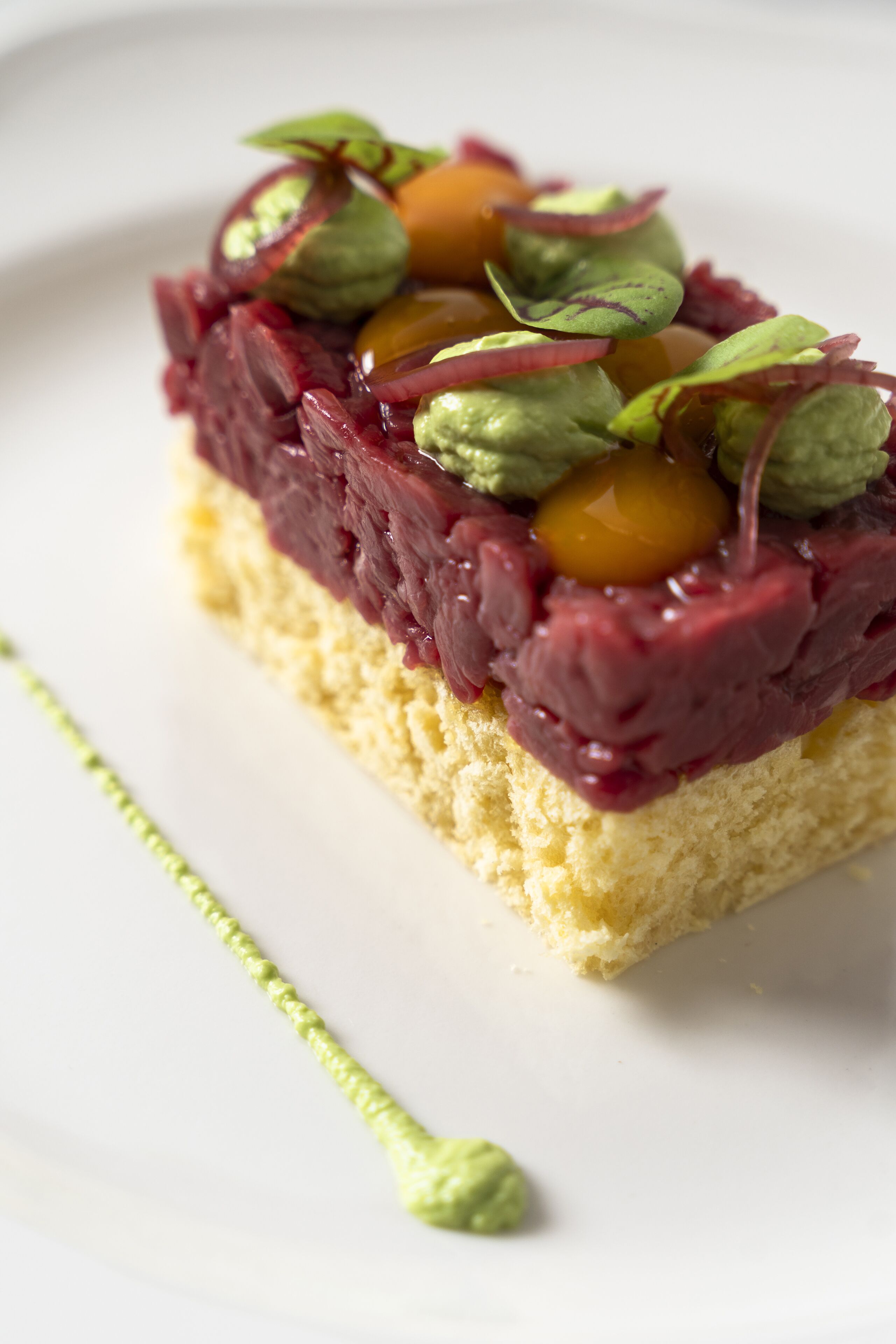 Ein Stück Kuchen mit cremiger Glasur und Früchtchen, serviert auf einem weißen Teller.