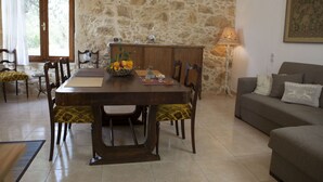 A dining area with a stone wall, wooden furniture, and a table set with fruits and a pitcher. - Horizonte Cretan Cottage (Kissamos)