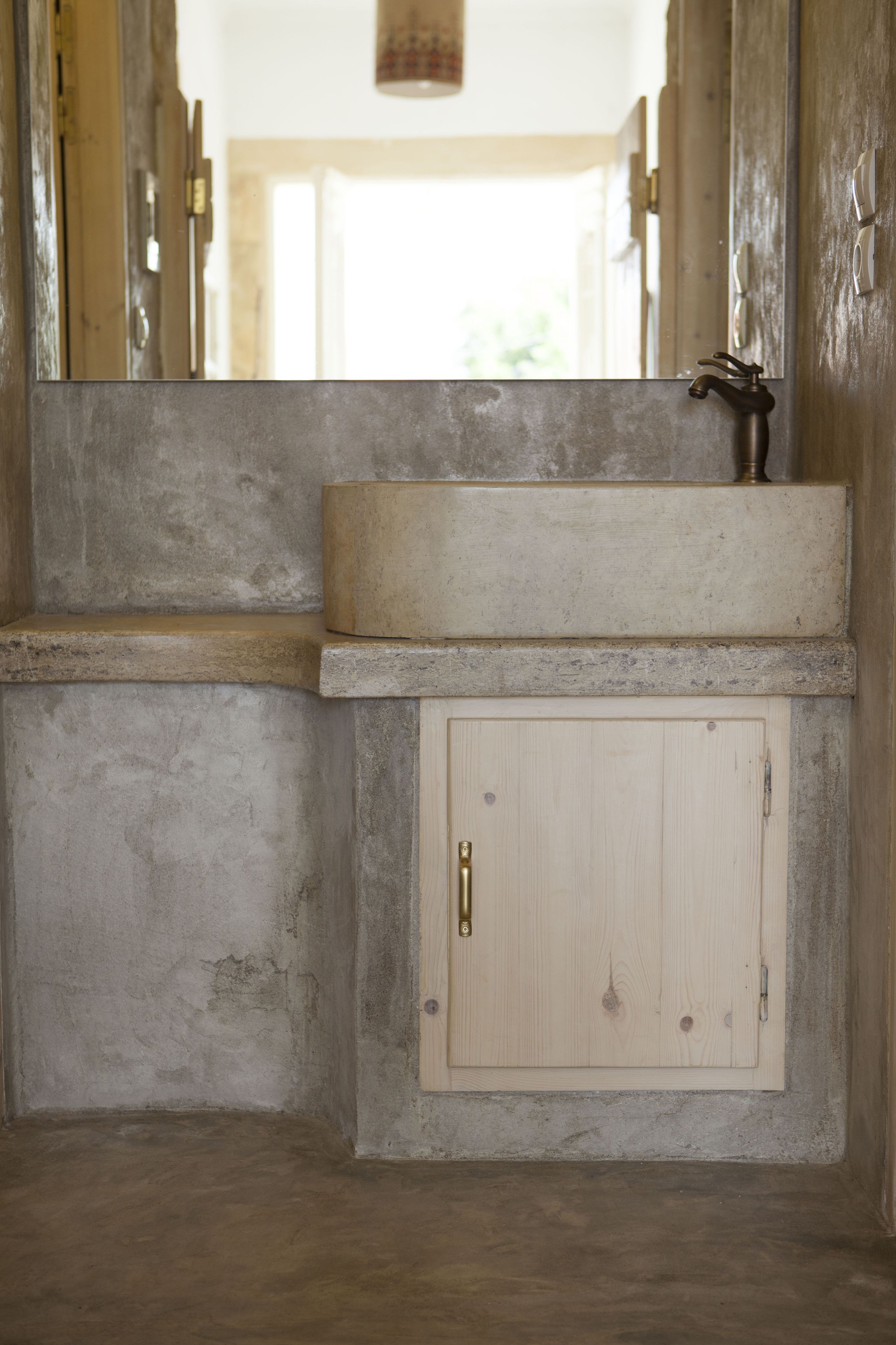 A bathroom with a concrete sink, wooden cabinet, and a view of a bright outdoor area.