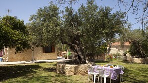 A stone building with a table and chairs set up outside, surrounded by trees. - Horizonte Cretan Cottage (Kissamos)