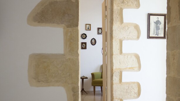 A hallway with a stone archway leading to a room with a green chair and framed pictures on the wall. - Horizonte Cretan Cottage (Kissamos)