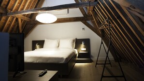 A bedroom with a wooden ceiling, a bed with white bedding, bedside lamps, and a remote control on the floor. - Hotel & Brasserie Katoen (Goes)