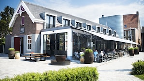 A restaurant with outdoor seating, a brick building, and large planters. - Hotel & Brasserie Katoen (Goes)