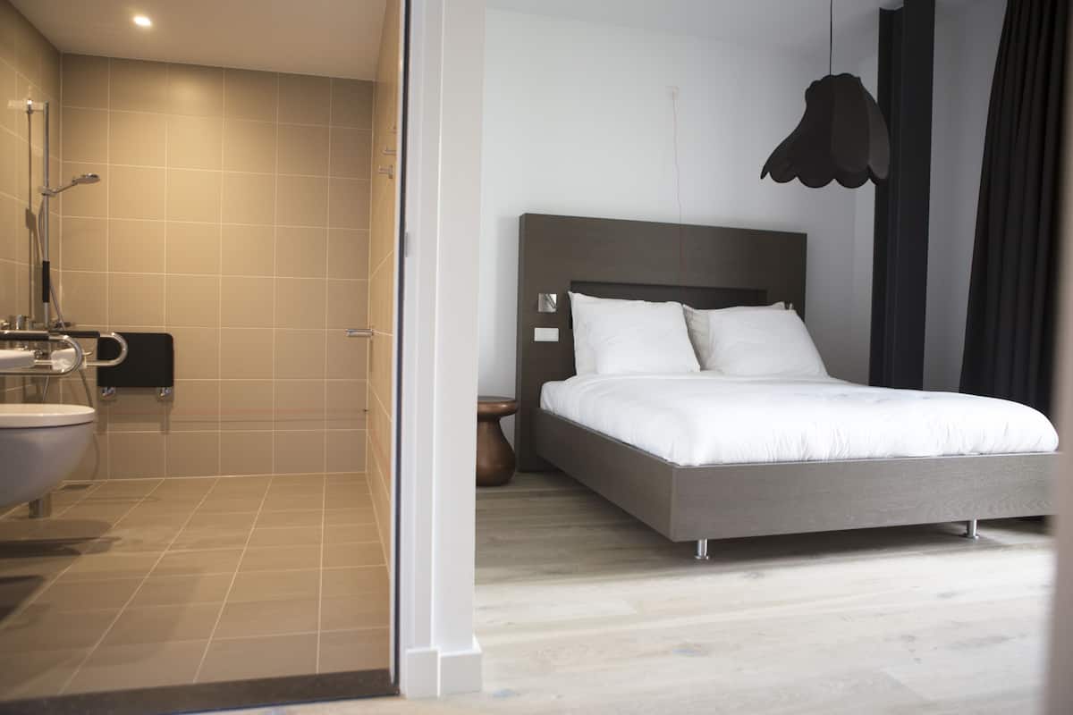 A modern hotel room with a large bed, a separate bathroom, and a shower area.
