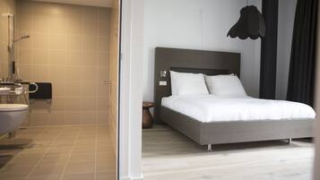 A modern hotel room with a large bed, a separate bathroom, and a shower area.