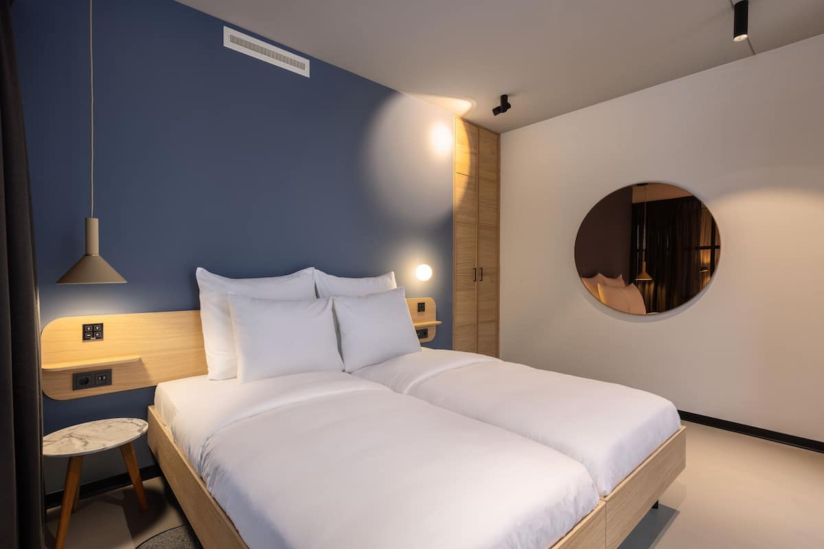 A modern bedroom with a double bed, bedside tables, a round mirror, and a small round table.