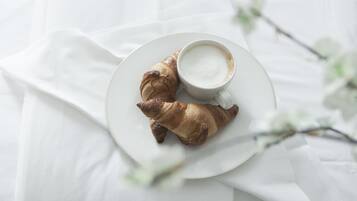 Un plato con dos cruasanes y una taza de café sobre un mantel blanco.