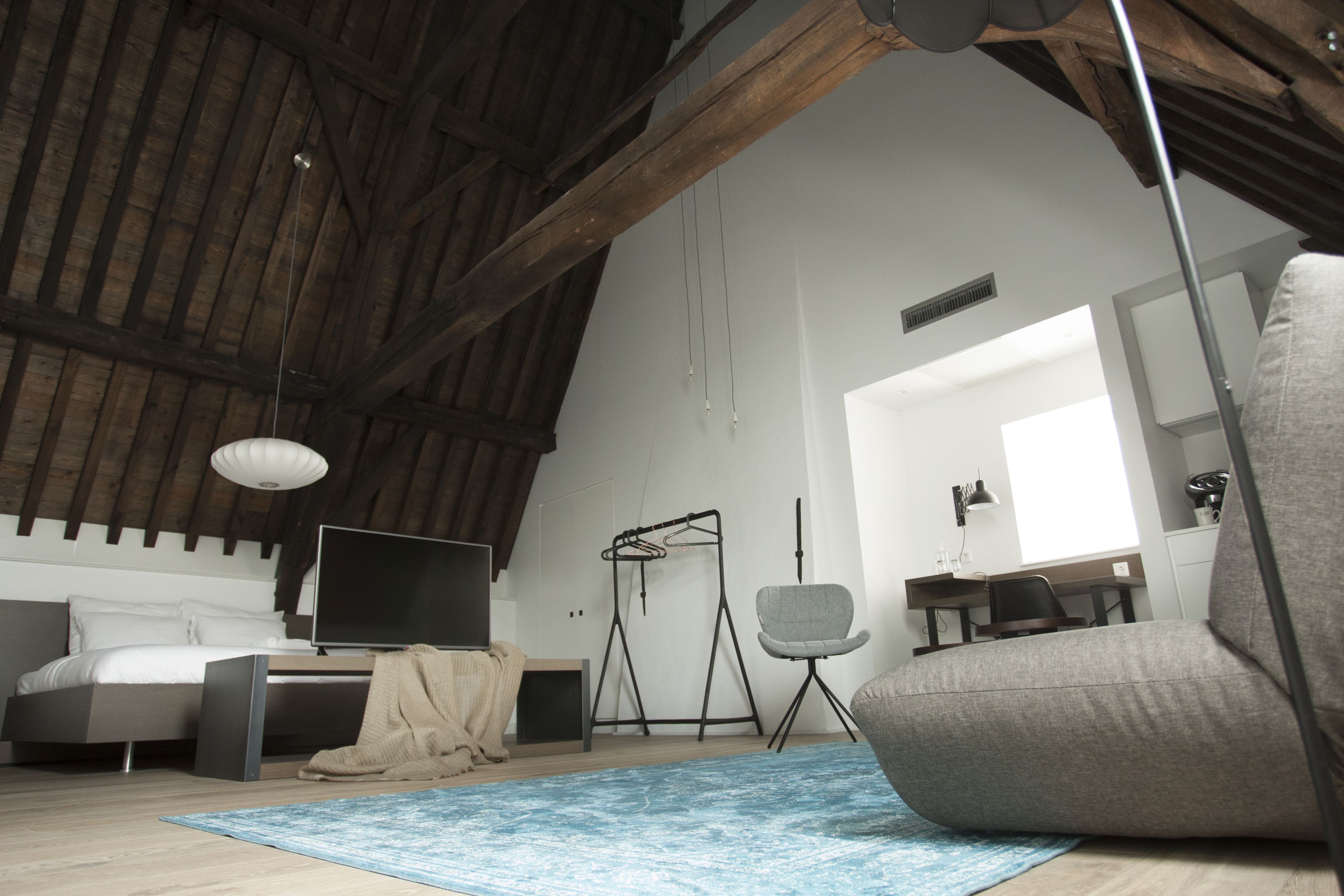 A spacious loft bedroom with a high ceiling, a bed, a desk, a chair, and a hanging light fixture.