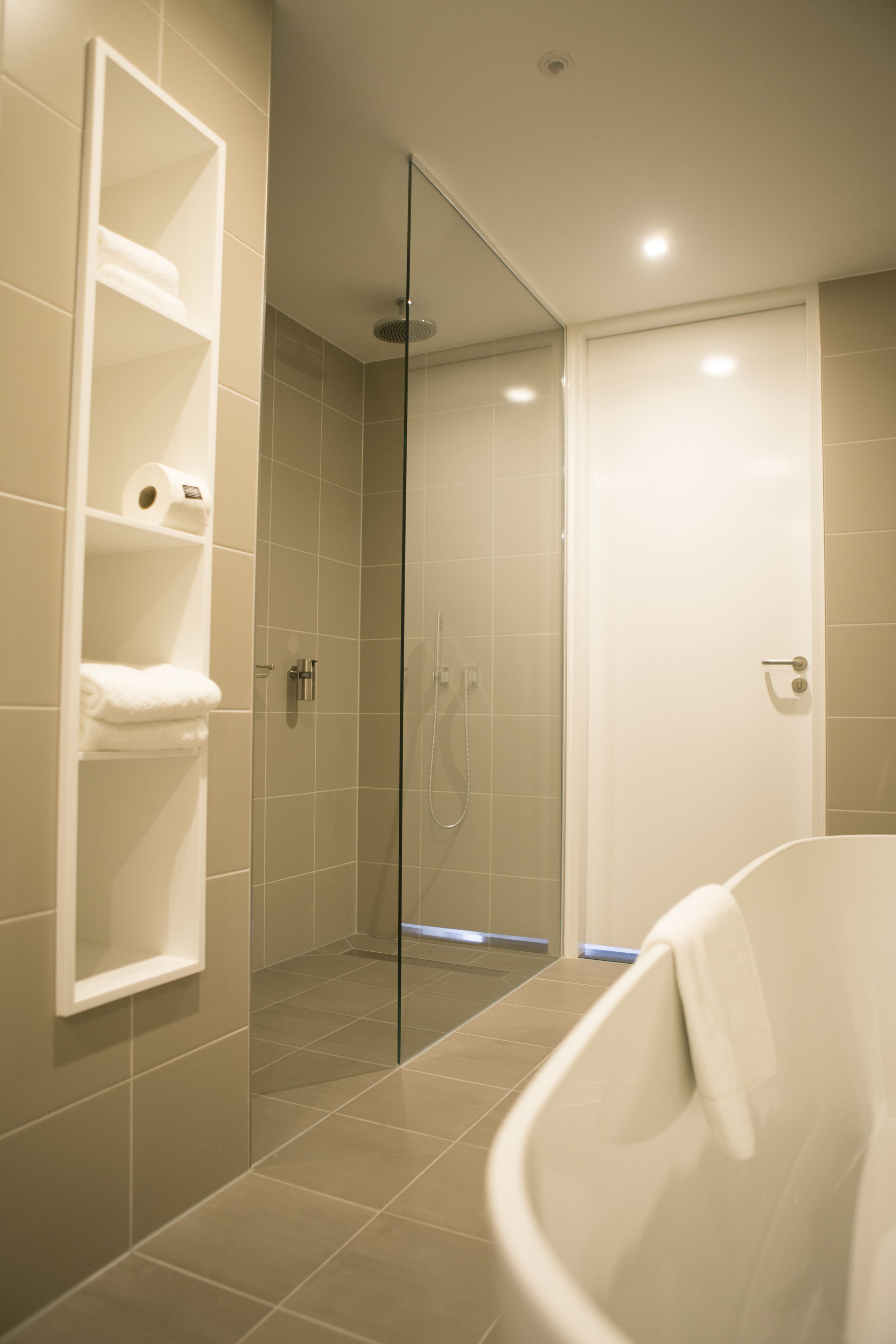 A modern bathroom with a glass-enclosed shower, a white bathtub, and a shelf with towels.