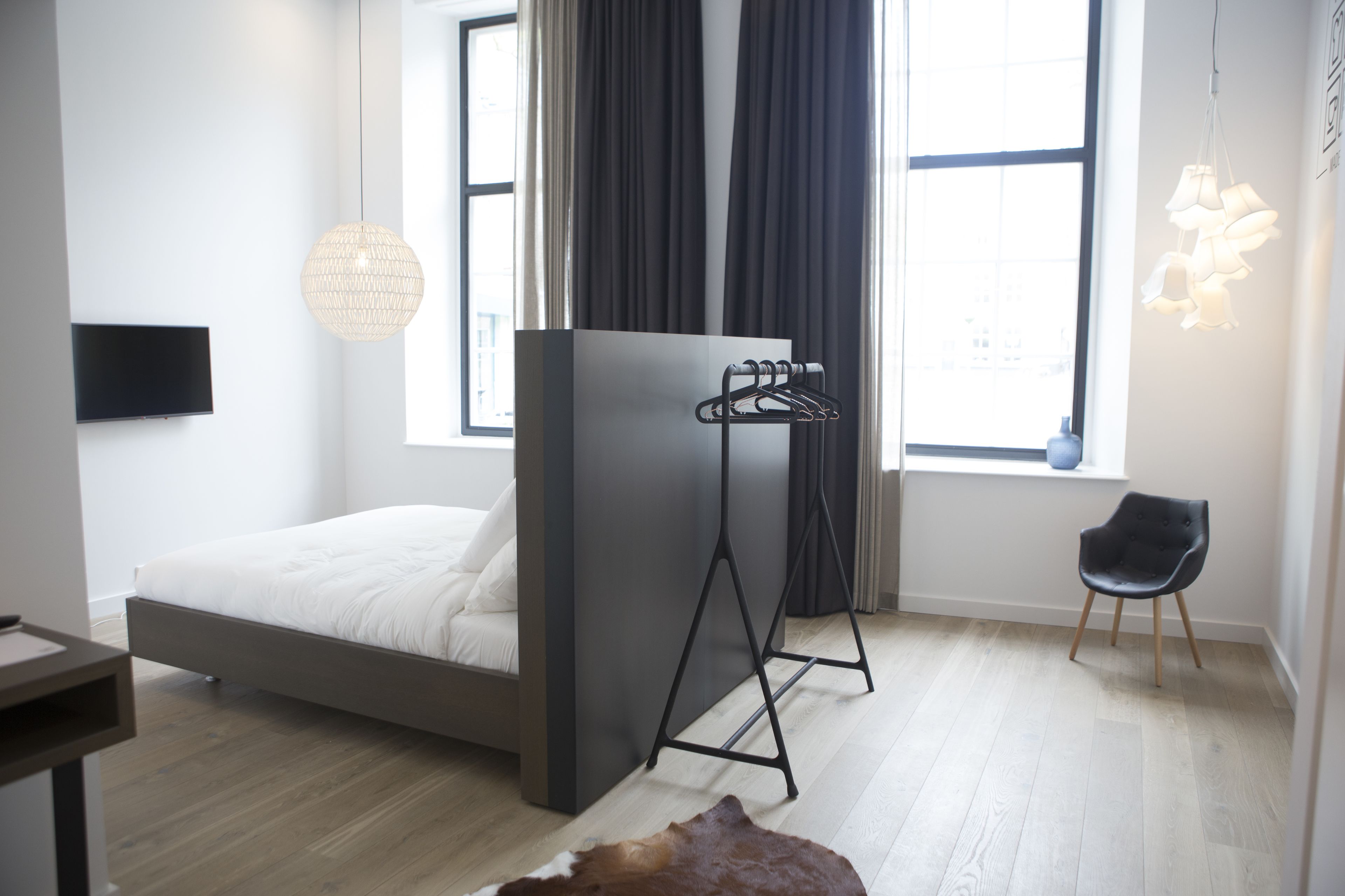 Un dormitorio moderno con cama, un perchero negro, una silla y un televisor en la pared.