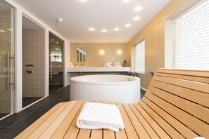 A modern bathroom with a large bathtub, wooden bench, and a glass shower enclosure. - Hotel & Brasserie Katoen (Goes)