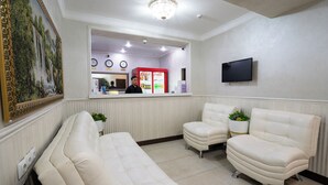 A reception area with a counter, a Coca-Cola refrigerator, a television, and two white leather sofas.