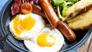 A skillet with breakfast items including sausages, eggs, and a side salad.