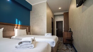 A hotel room with two beds, a wooden headboard, a small wooden side table, and a TV mounted on the wall.