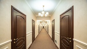 A hotel hallway with dark wooden doors, a carpeted floor, and a chandelier.