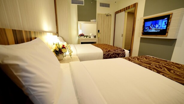 Een hotelkamer met twee bedden, een televisie aan de muur, een spiegel in de badkamer en een nachtkastje met bloemen.