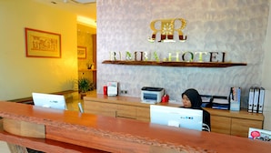 Een receptiebalie bij Rimba Hotel, met een houten toonbank, een receptionist en een bord aan de muur.