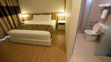 Ein Hotelzimmer mit Bett, Nachttisch und einem Badezimmer mit Toilette und Waschbecken.