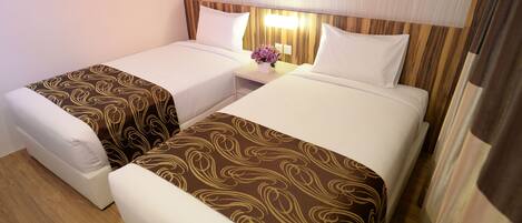 A hotel room with two single beds, a nightstand with a lamp, and a floral arrangement.