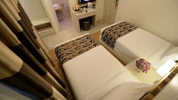 Two single beds with patterned bedspreads, a small desk with a television, and a bathroom in the background.