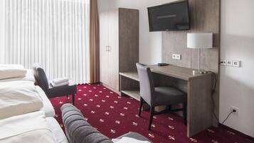 Una habitación de hotel con una cama, un escritorio con una silla, un televisor y una alfombra roja con diseño.