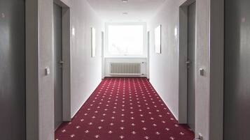 A hallway with a red carpet, white walls, and a window at the end.