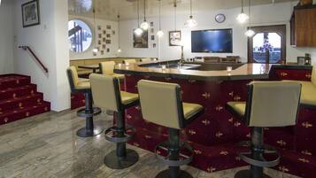 A bar area with a pool table, bar stools, and a television.