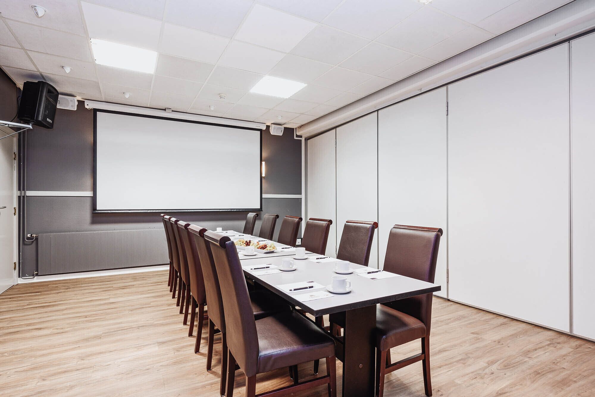 Una sala de conferencias con una mesa larga, sillas, una pantalla de proyector y una pizarra.